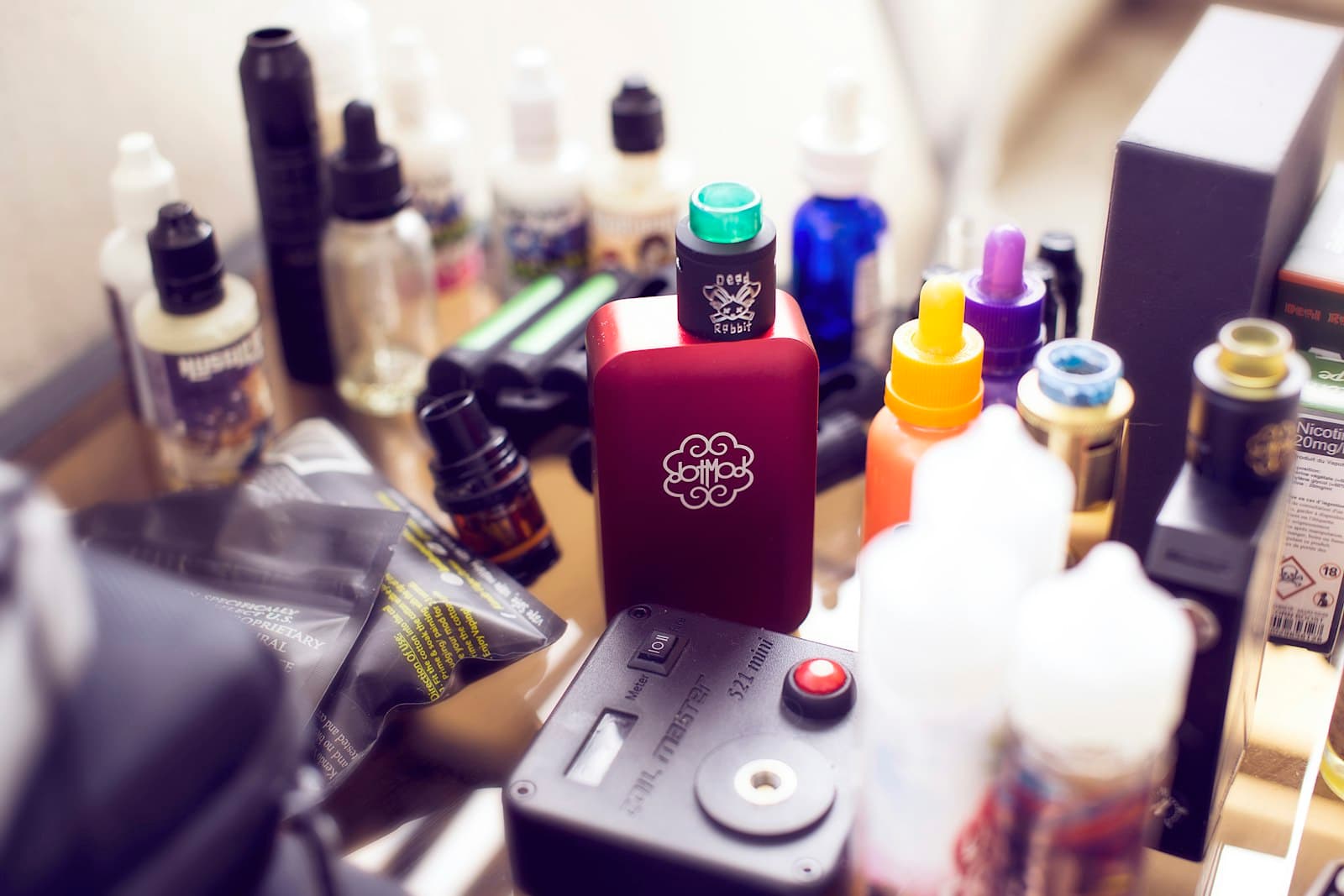 Red box mod device standing beside several e-liquid bottles on a table