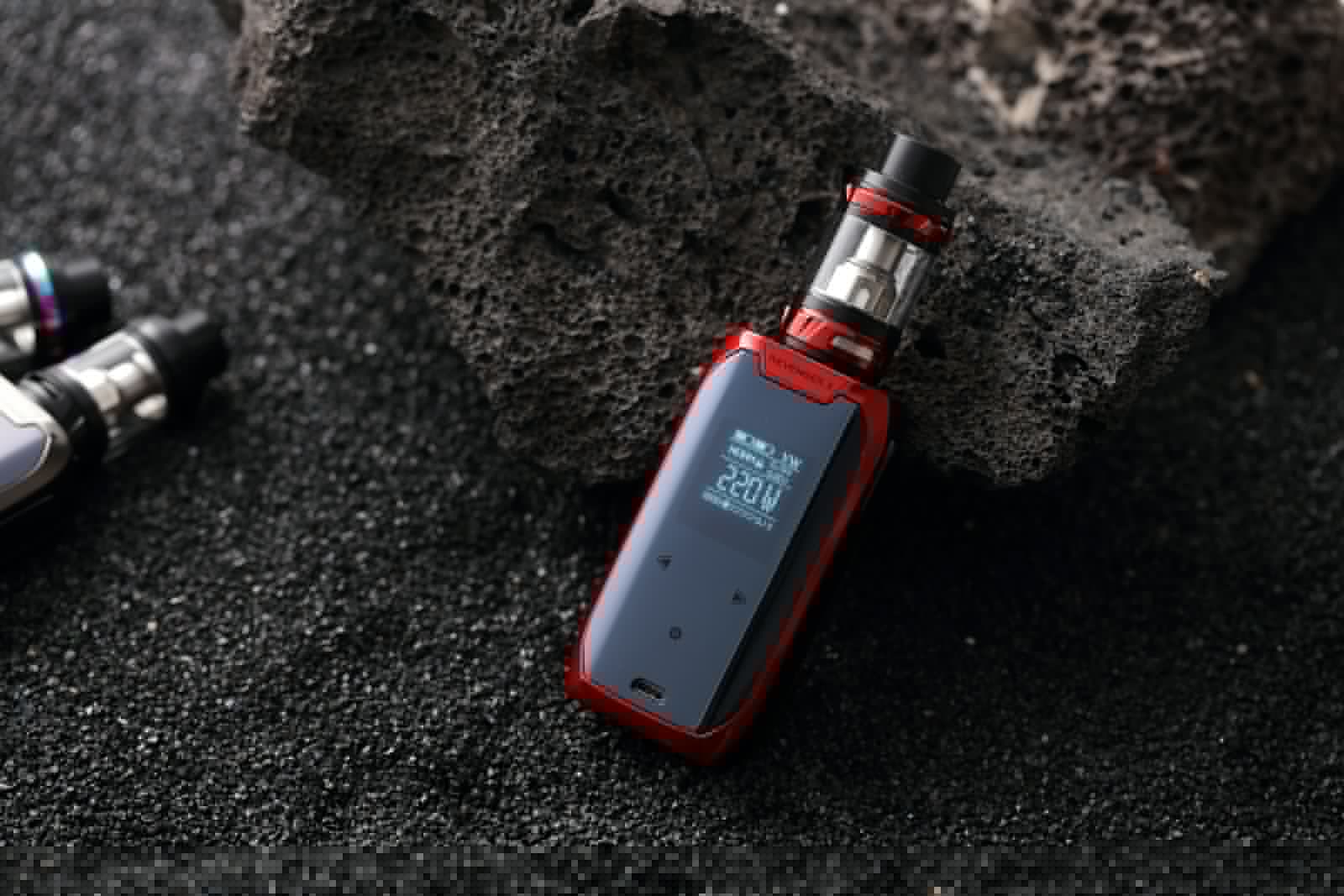 Red and black box mod device standing upright on a dark surface
